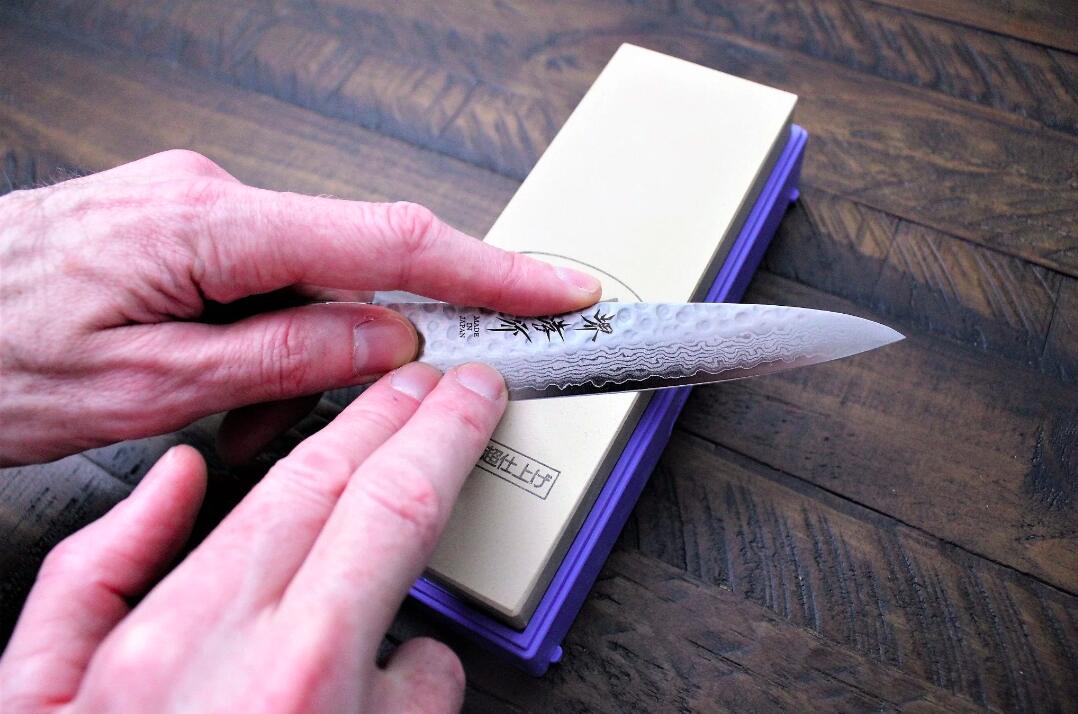 Hands sharpening a Japanese knife on a whetstone